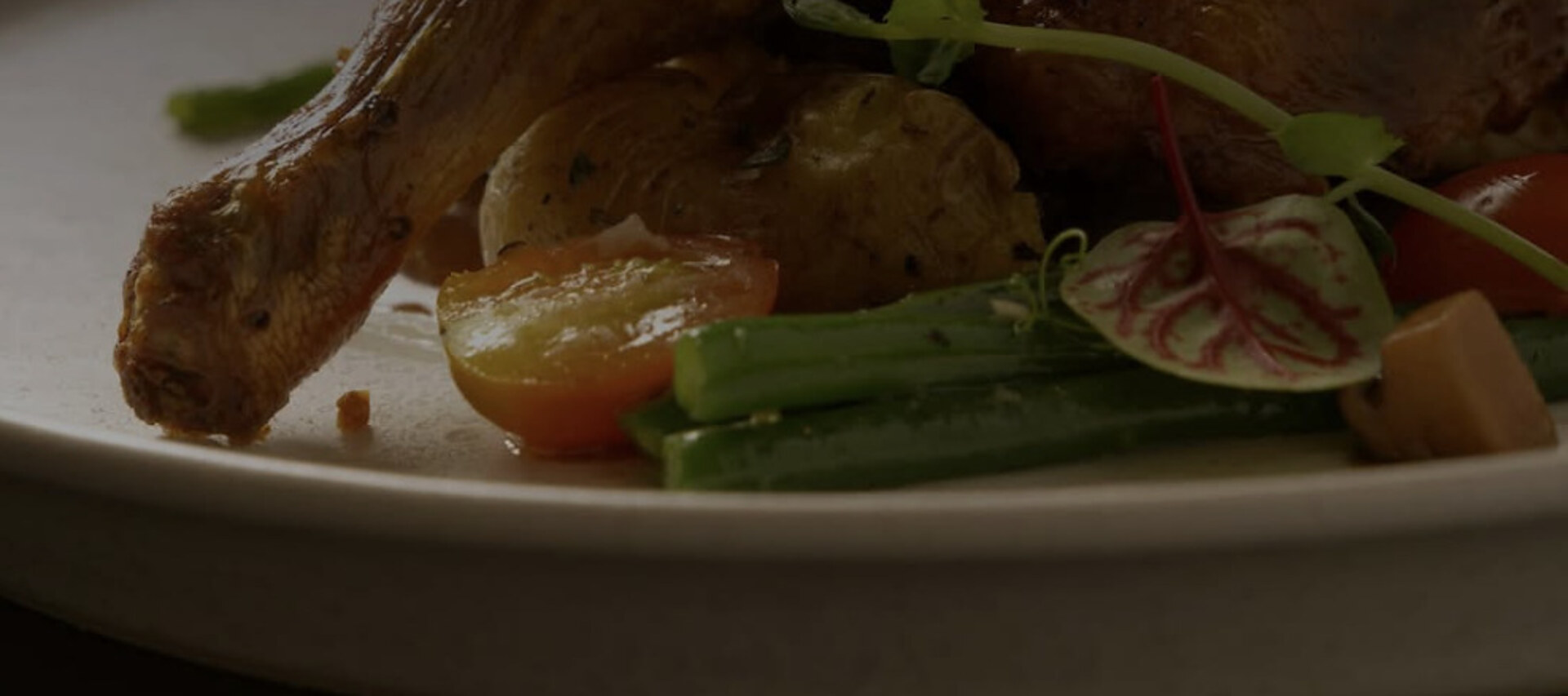 Close view of roast poultry with baby potatoes, green beans and herbs on a pale ceramic plate