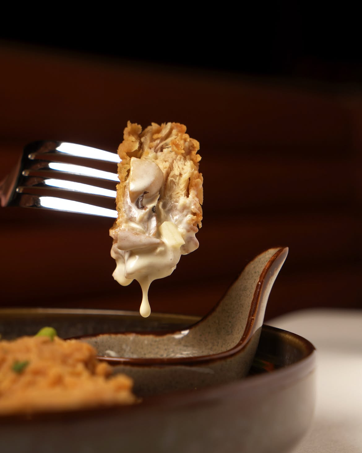 A fork lifting crisp chicken with creamy mushroom sauce