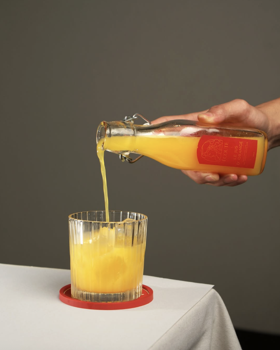 Fresh orange juice poured from an Écoute bottle into a ribbed glass